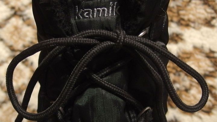 Ein schwarzer Schn&uuml;rsenkel ist ordentlich gebunden an einem Schuh. Die Umgebung zeigt einen weichen, hellen Teppich.