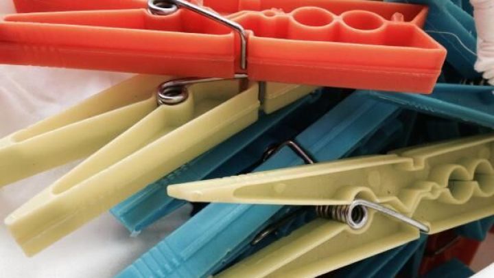 Bunte W&auml;scheklammern liegen auf einer wei&szlig;en Oberfl&auml;che und warten darauf, eine Tischdecke bei Wind zu beschweren.