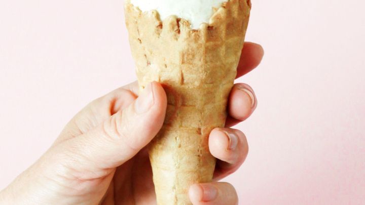 Eine Hand h&auml;lt eine Eist&uuml;te mit einer Kugel Eis, vor einem sanften, rosa Hintergrund, sie tropft nicht mehr.