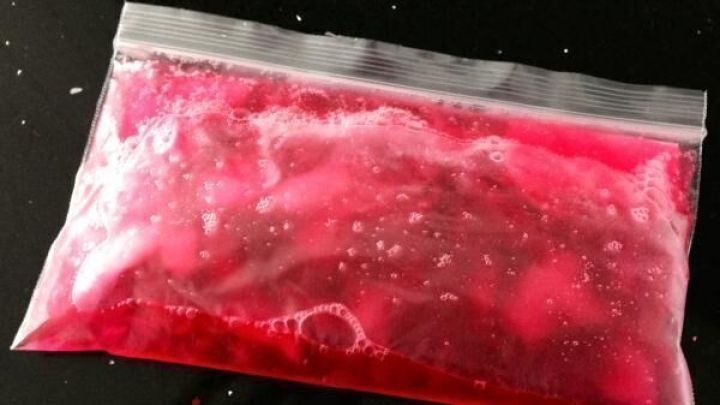 Ein roter Gel-Eisbeutel liegt auf schwarzem Untergrund, gef&uuml;llt mit geleeartiger Masse, die leicht sch&auml;umt.