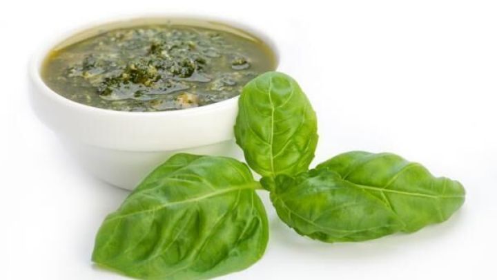 Eine Sch&uuml;ssel mit Pesto alla Genovese steht auf einem wei&szlig;en Hintergrund, umgeben von frischen Basilikumbl&auml;ttern.
