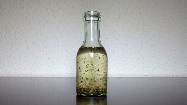 Eine klare &Ouml;lflasche steht auf einer glatten Oberfl&auml;che und reflektiert das Licht, w&auml;hrend sie mit goldenem &Ouml;l gef&uuml;llt ist.