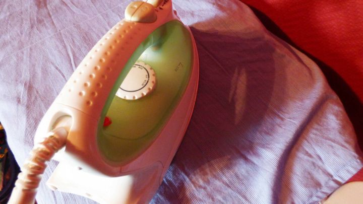 Ein B&uuml;geleisen liegt auf einem blauen Hemd, w&auml;hrend es f&uuml;r das B&uuml;geln von Falten in einem gem&uuml;tlichen Raum vorbereitet wird.