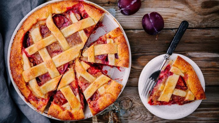 Ein Pflaumenmuskuchen steht auf einem rustikalen Holztisch, mit einem St&uuml;ck auf einem Teller daneben, bereit zum Genie&szlig;en.