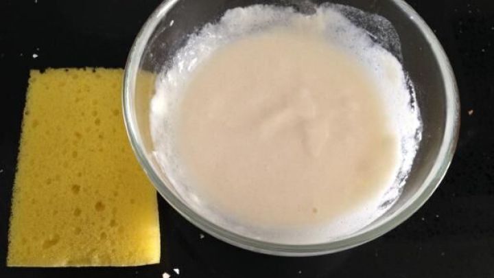Eine Schale mit selbstgemachter Scheuermilch steht auf einem dunklen Tisch, daneben liegt ein gelber Schwamm.