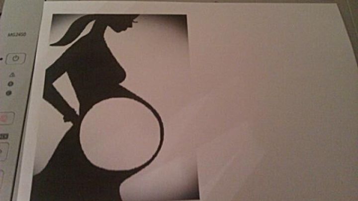 Silhouette einer schwangeren Frau auf Papier liegt auf einem Drucker, betont eine dekorative Darstellung der Schwangerschaft.