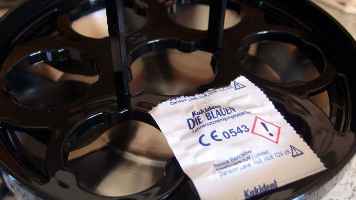 Eine schwarze Heizplatte eines elektrischen Eierkochers liegt auf einer K&uuml;chenoberfl&auml;che mit einem Sicherheitsetikett.