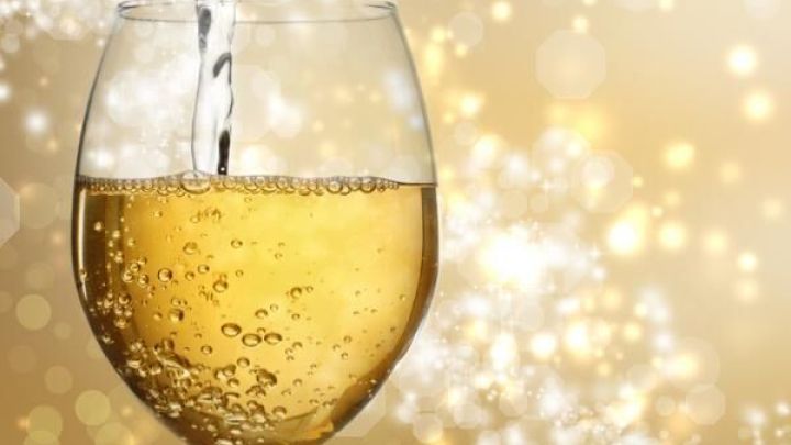 Ein Glas mit sprudelndem Wei&szlig;wein wird eingegossen, umgeben von einem goldenen, funkelnden Hintergrund.