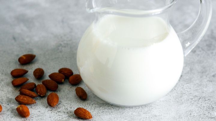 Ein Glas Mandelmilch steht auf einer grauen Oberfl&auml;che neben einigen Mandeln, symbolisiert ihre Anwendung gegen Sodbrennen.