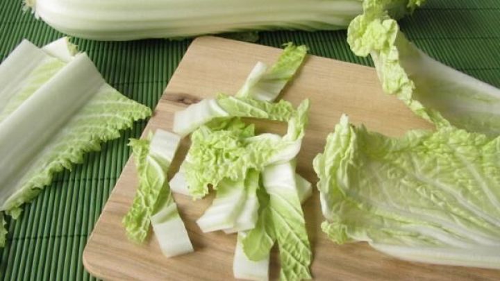 Chinakohl wird auf einem Schneidebrett in Streifen geschnitten, umgeben von weiteren Bl&auml;ttern auf einer gr&uuml;nen Matte.
