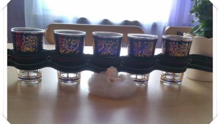 Gl&auml;ser stehen in einer aufwendigen Halterung aus Leder auf einem Tisch, daneben eine kleine Figur auf Watte, im Licht eines Fensters.