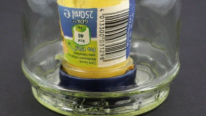 Eine umgedrehte Flasche steht stabil in einem Glas, das als Halterung dient, um ein Umfallen zu verhindern.