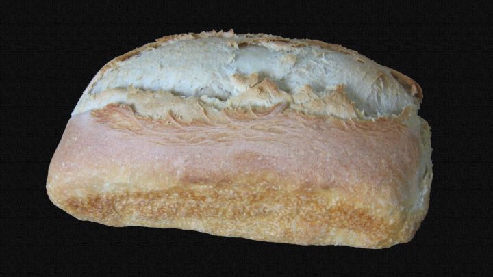 Ein frisch gebackenes Weizenbrot liegt auf einem dunklen Hintergrund und strahlt eine goldene, knusprige Kruste aus.