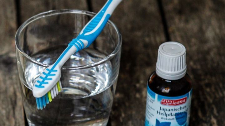 Ein Glas Wasser steht auf einem Holztisch, w&auml;hrend eine Zahnb&uuml;rste und ein Fl&auml;schchen Mundwasser daneben liegen.