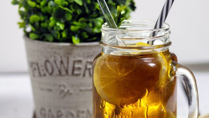 Ein dekoratives Glas mit einem goldbraunen Getr&auml;nk und einem Strohhalm steht neben einem Pflanzentopf auf einem Tisch.