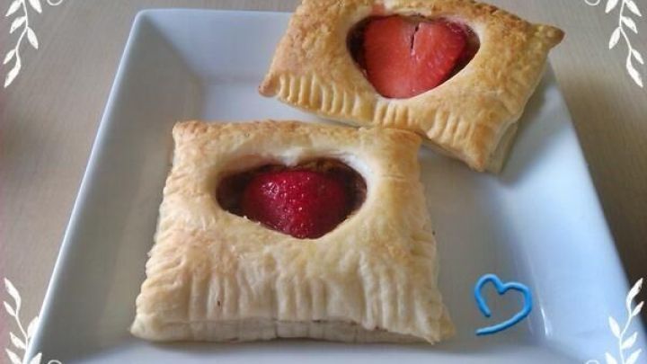 Zwei Bl&auml;tterteigtaschen liegen auf einem wei&szlig;en Teller, gef&uuml;llt mit Schokolade und frischen Erdbeeren.