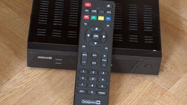 Eine TV-Fernbedienung liegt auf einem SAT-Receiver auf einem Holzfu&szlig;boden, bereit zur Nutzung ohne direkten Kontakt.