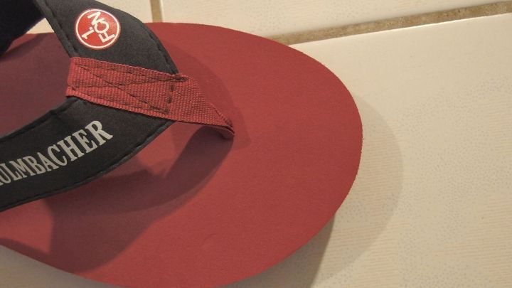 Ein roter Flip-Flop steht auf einem hellen Fliesenboden, ideal f&uuml;r die Fu&szlig;hygiene zur Vorbeugung von Fu&szlig;pilz.