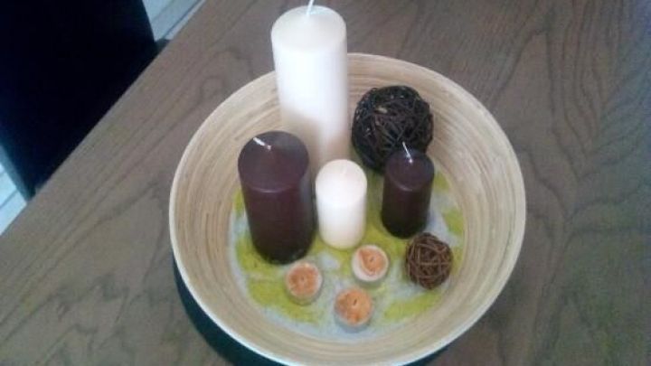 Kerzen in verschiedenen Gr&ouml;&szlig;en und Farben stehen in einer Holzschale auf einem Holztisch, umgeben von Deko-Kugeln.