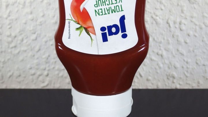 Eine Ketchupflasche steht aufrecht auf einem Tisch und scheint bereit zum Ausgie&szlig;en des Tomatenketchups.