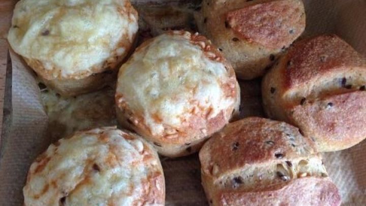 Br&ouml;tchen liegen knusprig auf einem Holzbrett, frisch gebacken mit K&auml;se und K&ouml;rnern, und laden zum Essen ein.