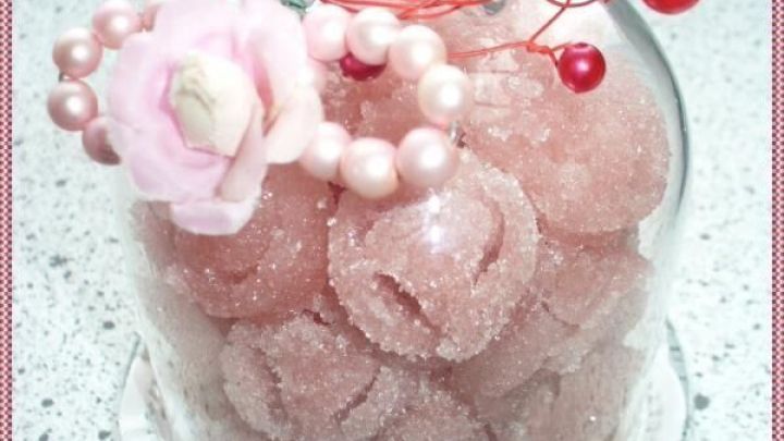 Zuckrige Erdbeer- und Himbeerzuckerrosen sind in einer Glasglocke angeordnet, dekoriert mit Perlen und einer Bl&uuml;te.