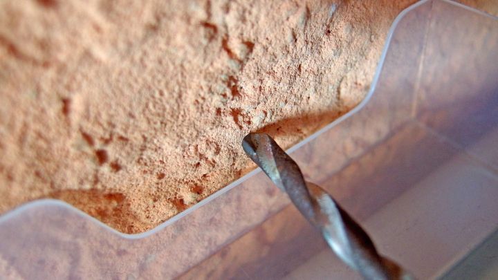 Ein Bohrer bohrt in eine Wand, w&auml;hrend ein Staubschutzbeh&auml;lter ihn umgibt, um Staub auf dem Boden zu vermeiden.