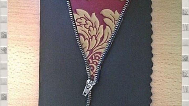 Eine schwarze Karte mit einem Rei&szlig;verschluss, der ge&ouml;ffnet ist und ein dekoratives Innenmaterial zeigt. Darunter steht "ALLES GUTE" mit einem kleinen Herz.