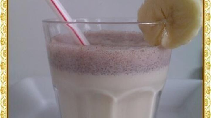 Ein Glas Milchshake mit Bananenscheibe und rot-wei&szlig;em Strohhalm steht auf einem wei&szlig;en Teller.