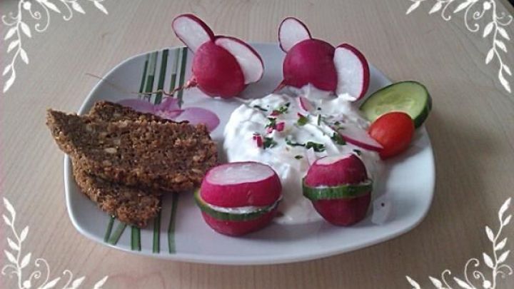 Radieschen und ein cremiger Aufstrich sind auf einem Teller arrangiert, umgeben von Vollkornbrot und frischem Gem&uuml;se.