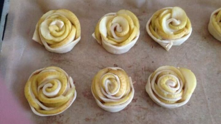 Apfelrosen in Plunderteig auf einem Backblech, bereit zum Backen. Die Rosenform entsteht durch gerollte Apfelscheiben.