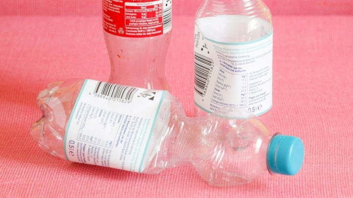 Zerdr&uuml;ckte PET-Flaschen liegen auf einer pinken Fl&auml;che, einige stehen aufrecht, andere sind flach gepresst.