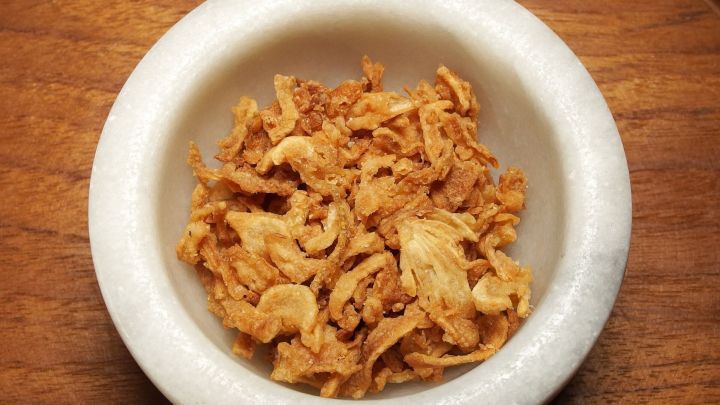 Krosse R&ouml;stzwiebeln liegen in einer wei&szlig;en Schale auf einem Holztisch, bereit, Gulasch oder &auml;hnliches zu verfeinern.