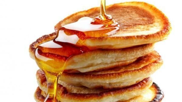 Ahornsirup flie&szlig;t &uuml;ber einen Stapel goldener Pfannkuchen, die aufeinander gestapelt sind, vor wei&szlig;em Hintergrund.