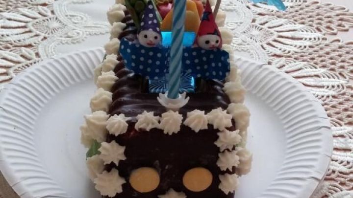 Schokoladen-Kastenkuchen mit Sahnetupfen und Zierfiguren, dekoriert mit Kerzen und Schirmchen, auf Spitzendeckchen.