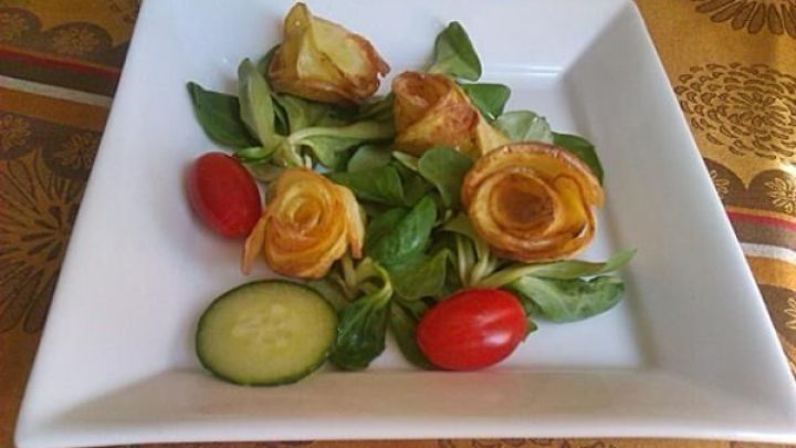 Frittierte Kartoffelrosen ruhen auf Feldsalat mit Cherrytomaten und Gurkenscheibe auf einem wei&szlig;en quadratischen Teller.