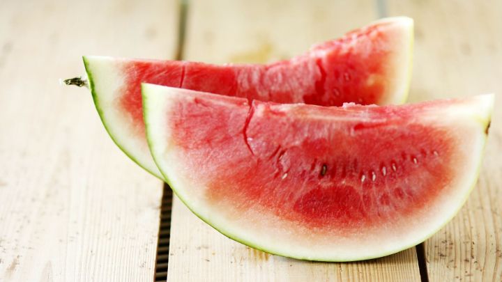 Reife Wassermelonenst&uuml;cke liegen auf einem Holzbrett und zeigen saftiges, rotes Fruchtfleisch.