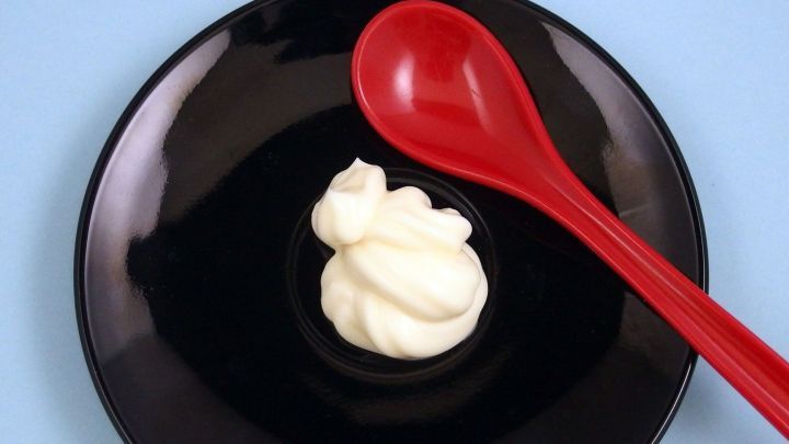 Eine rote L&ouml;ffel liegt neben einem essbaren, wei&szlig;en Klecks Mayonnaise ohne Ei auf einem schwarzen Teller.