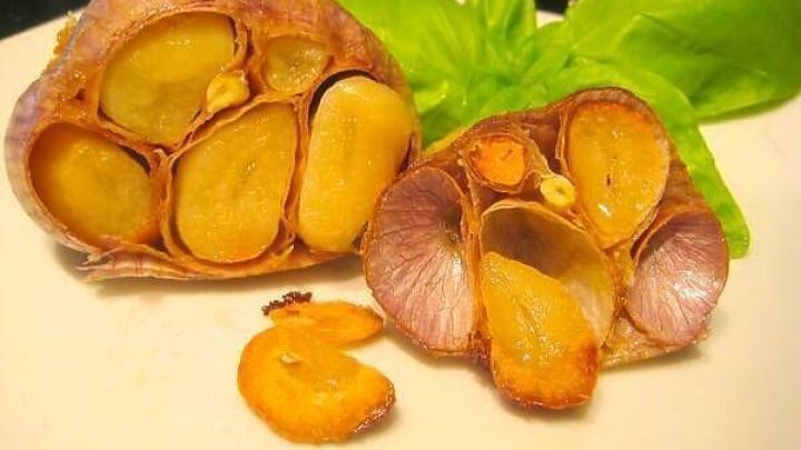 Gebackener Knoblauch liegt auf einem Teller, einige Zehen sind halbiert und leicht goldbraun, umgeben von frischem Basilikum.