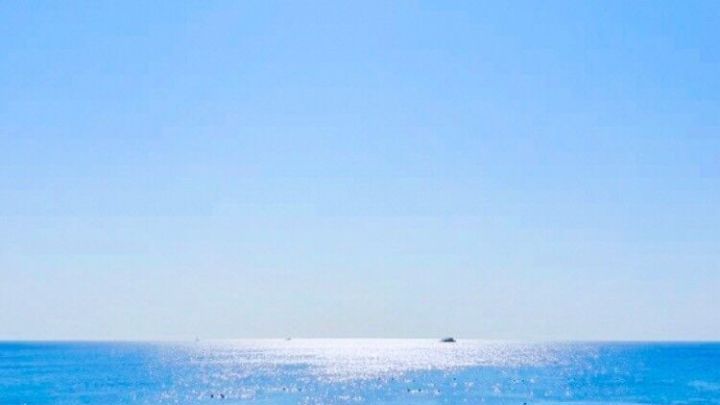 Strandliegen mit Sonnenschirmen stehen am Sandstrand, w&auml;hrend die Sonne &uuml;ber dem glitzernden Wasser strahlt.
