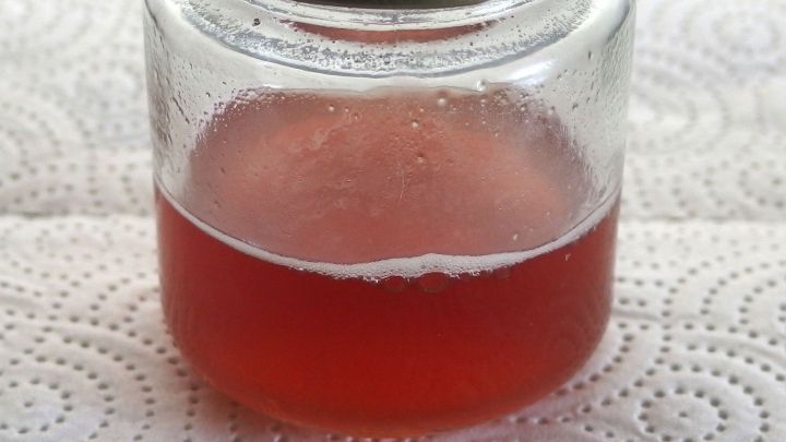 Ein Marmeladeglas mit einer roten Fl&uuml;ssigkeit darin wird einfach ausgesp&uuml;lt und steht auf einem K&uuml;chentuch.