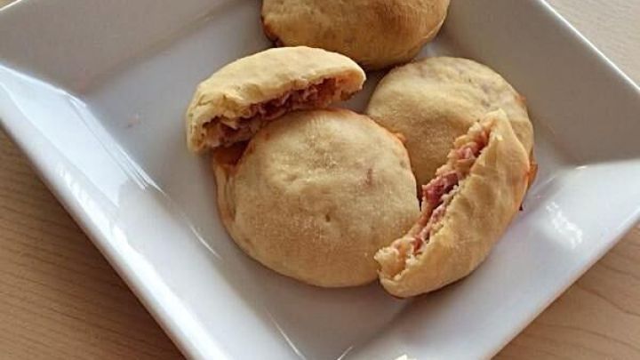 Drei goldbraune Calzone Br&ouml;tchen liegen auf einem wei&szlig;en Teller, wobei eines aufgebrochen und die F&uuml;llung sichtbar ist.