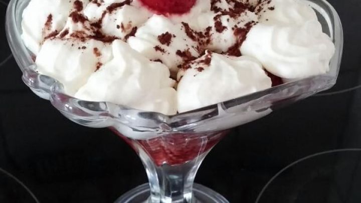 Ein Dessert besteht aus Erdbeeren und Schlagsahne, dekoriert mit Schokolade und einem Minzblatt, serviert in einem Glas.