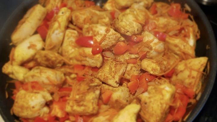 Saftiges H&auml;hnchenbrustfilet br&auml;t in einer Pfanne mit roten Paprika und Karottenstreifen, w&uuml;rzig und dampfend.