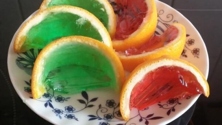 Bunte G&ouml;tterspeise-Fruchtschnitten in Orangenschalen auf einem Teller, die frisch zubereitet und appetitlich angerichtet sind.