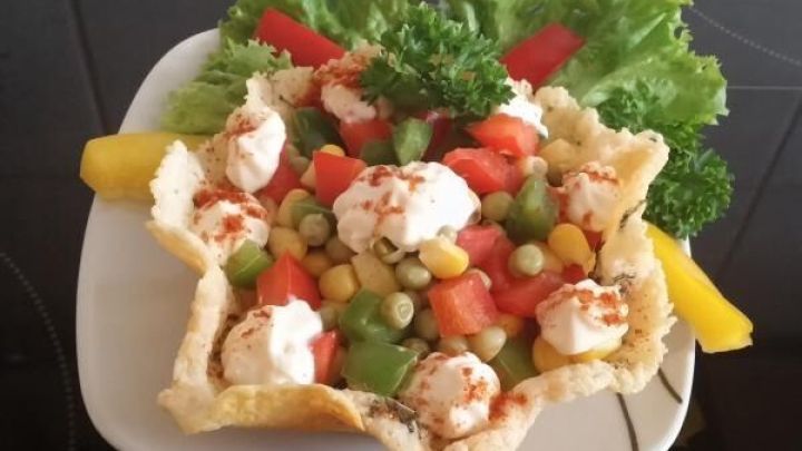 Ein gefaltetes K&ouml;rbchen aus knusprigem Teig h&auml;lt eine bunte Mischung aus Gem&uuml;se und Kr&auml;utern, pr&auml;sentiert auf einem Teller.