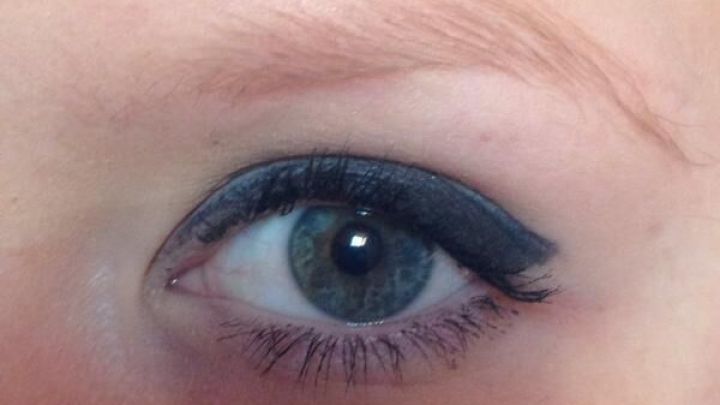 Ein Augenpaar wird von geschminkten Augenbrauen und feinem Eyeliner in einem gut beleuchteten Raum umrahmt.