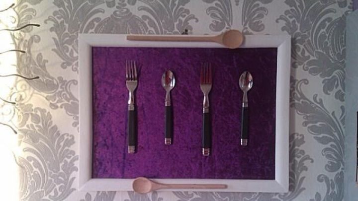 Besteck h&auml;ngt stilvoll in einem wei&szlig;en Rahmen an einer gemusterten Tapete; L&ouml;ffel oben und unten rahmen ein.