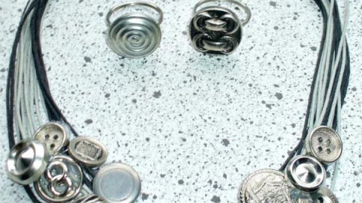 Ein einzigartiger Schmuck aus alten Kn&ouml;pfen zeigt eine Statementkette und passende Fingerringe auf einer grauen Oberfl&auml;che.