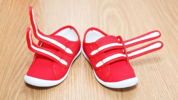 Rote Kinderschuhe mit offenen Klettverschl&uuml;ssen liegen auf einem hellen Holzboden und sind bereit, angezogen zu werden.